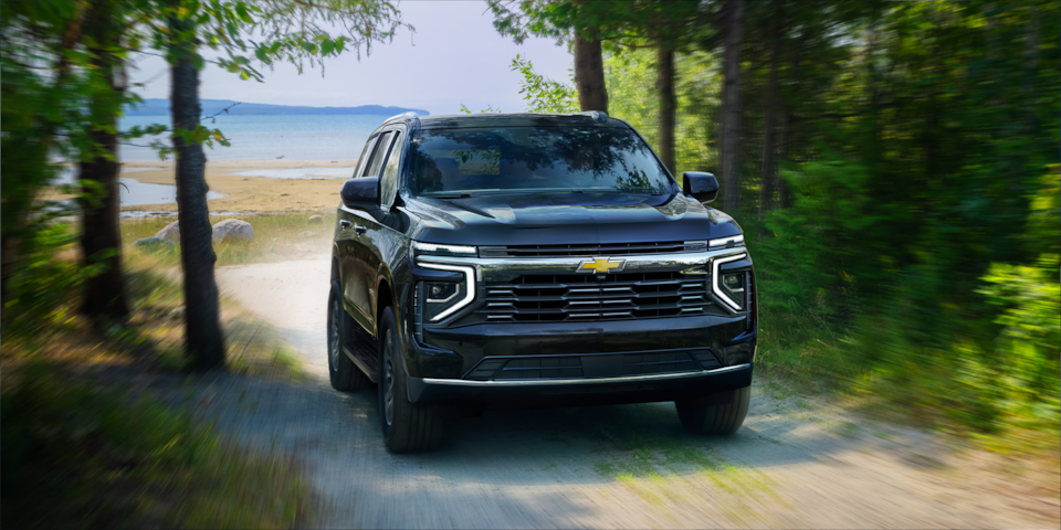 Front Three-quarters View of the 2025 Chevrolet Tahoe SUV Driving on a Gravel Path Surrounded by Trees