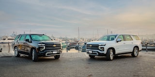 Front Three-quarters View of two 2025 Chevrolet Tahoe SUV's parked on gravel surface by a harbor