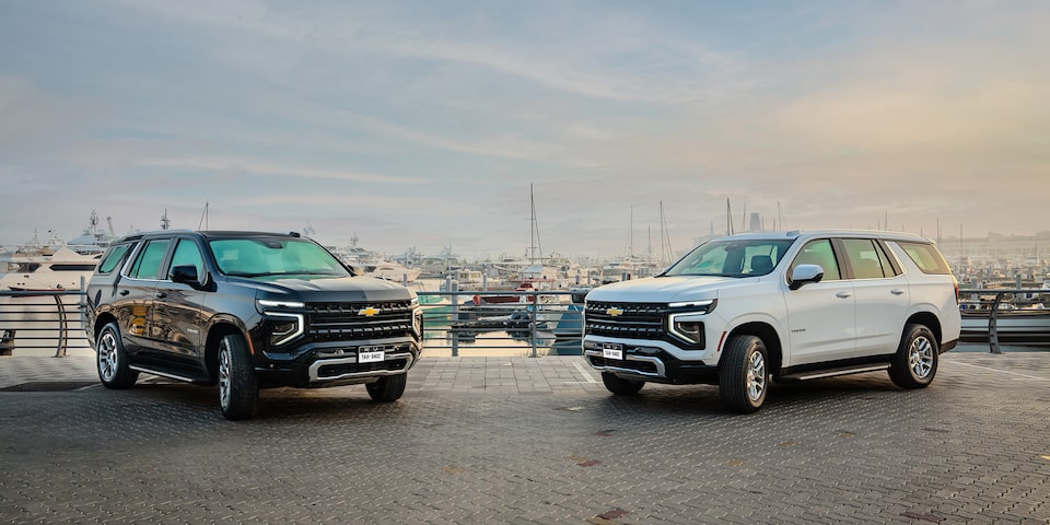 Front Three-quarters View of two 2025 Chevrolet Tahoe SUV's parked on gravel surface by a harbor