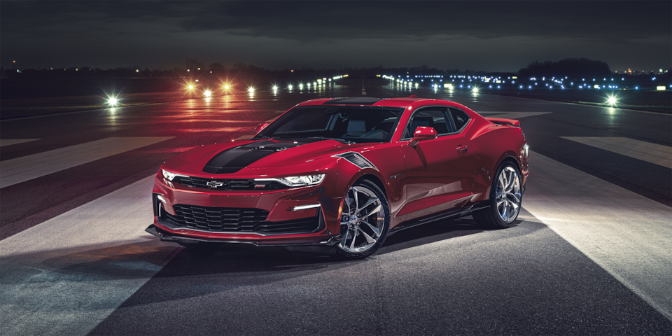 A Red With Black Racing Stripes 2024 Chevy Camaro Parked On Airplane Tarmac At Night